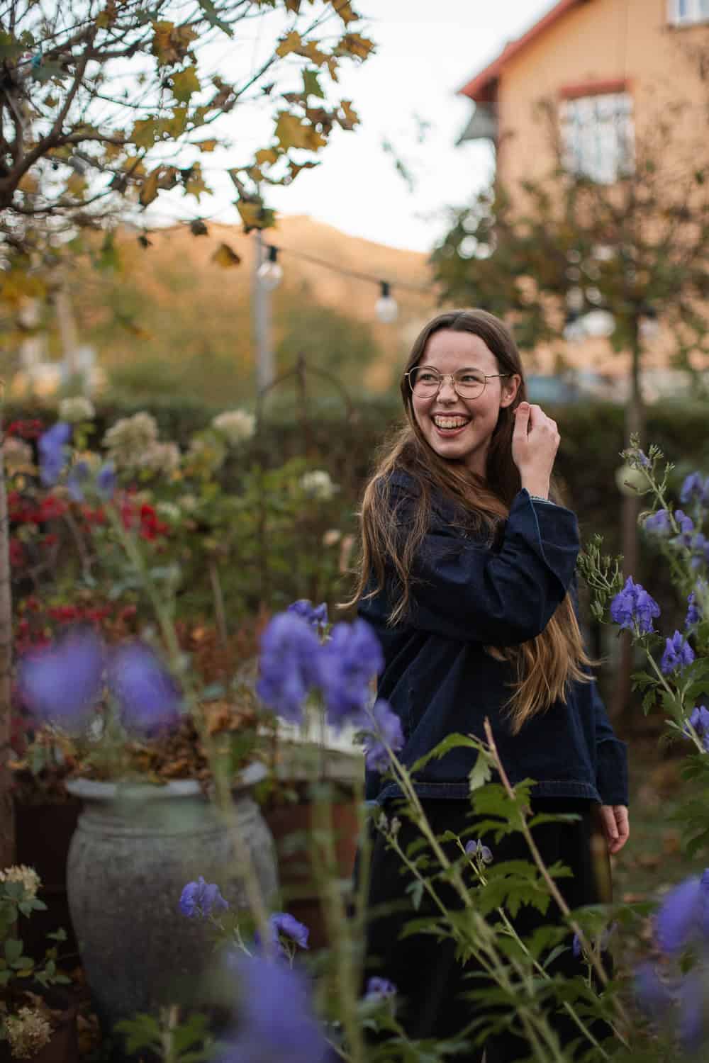 Smilende kvinne i blomsterhage med fargerike blomster og høstfarger.