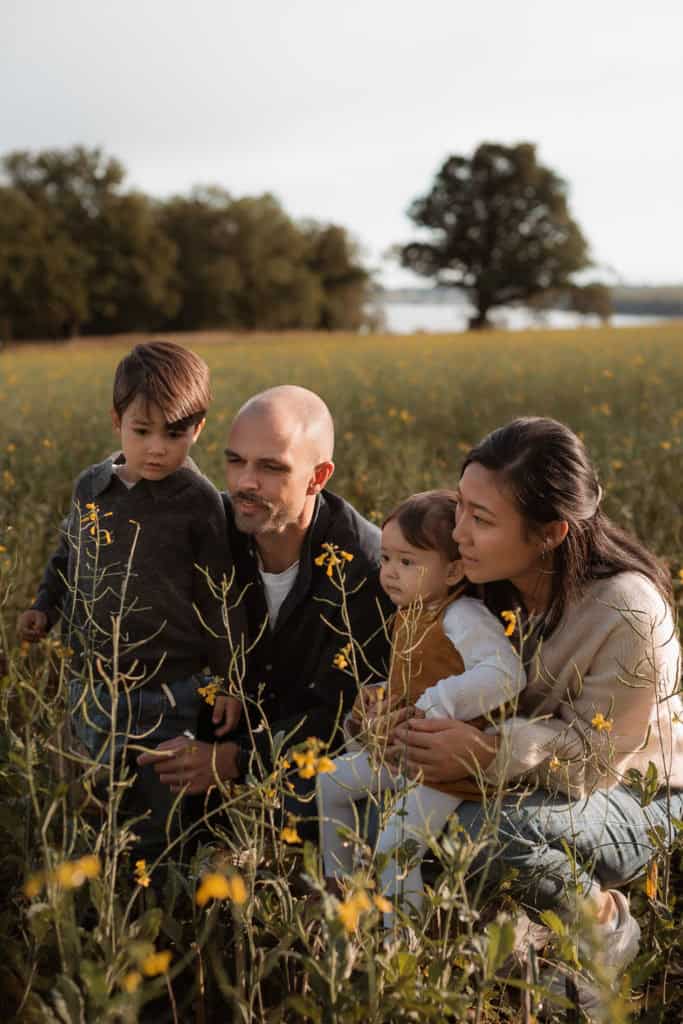 Bilde av familie i blomstereng med sesongens blomster og trær i bakgrunnen.