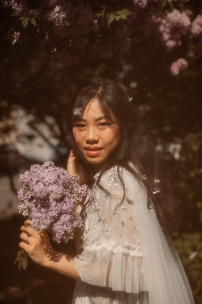 Nydelig jente med sesongens blomster i hender, omgitt av blomstrende trær. Perfekt for sesongens blo.