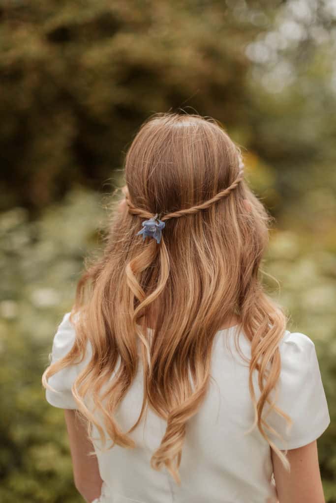 Bilde av en jente med langt, bølget hår og hårbånd, tatt utendørs i en grønn, naturlig setting.