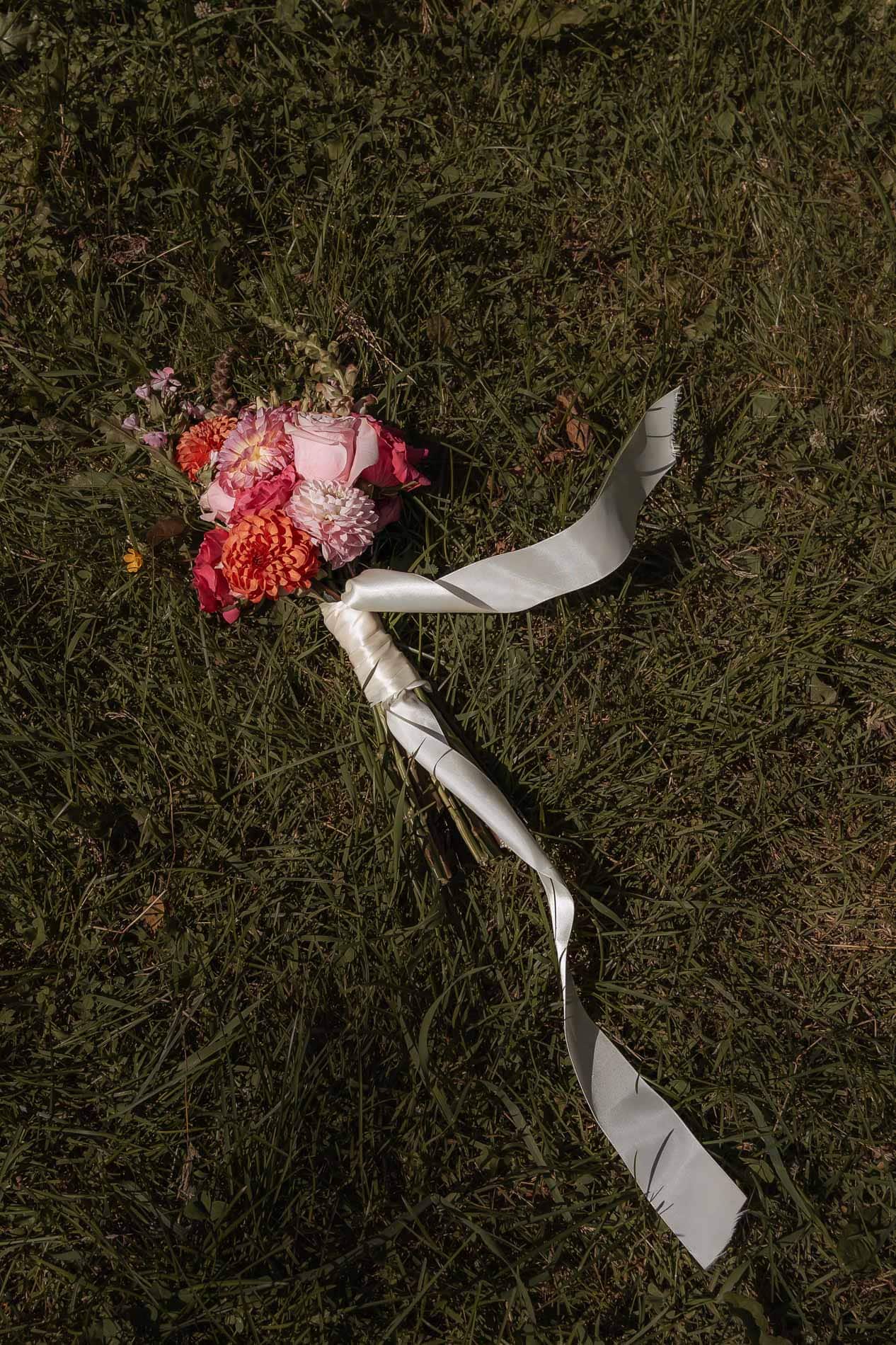 Blomsterbukett med rosa, hvite og oransje blomster på gresset, dekorert med hvit satengbånd.