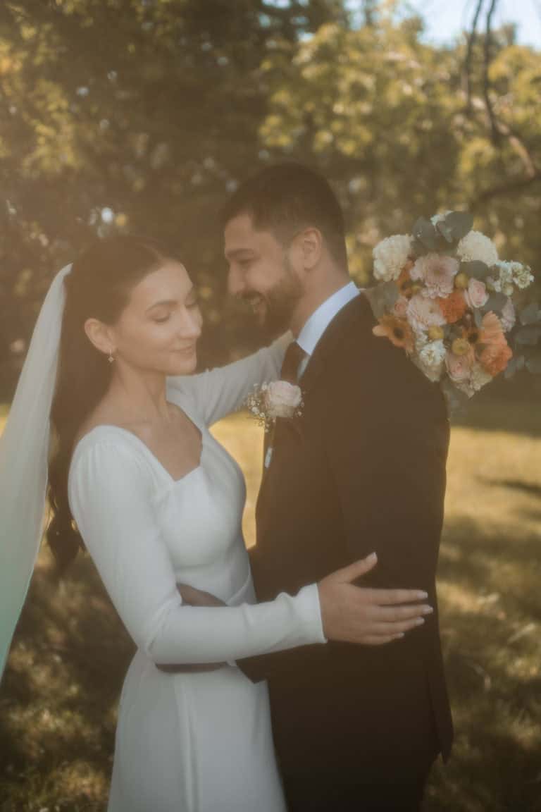 Bryllupsfoto av et lykkelig brudepar i en park, med blomster og solskinn.