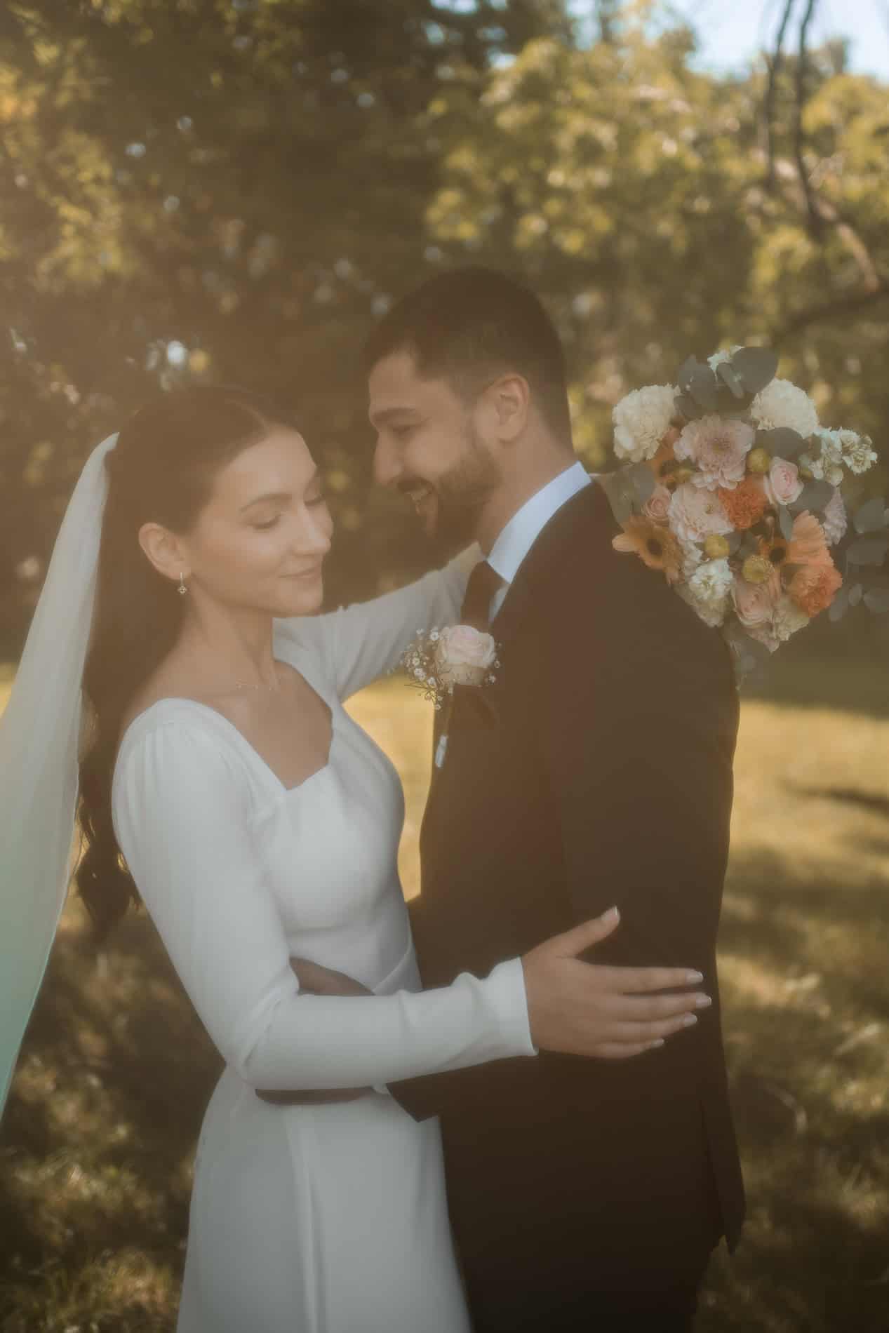 Bryllupsfoto av et lykkelig brudepar i en park, med blomster og solskinn.