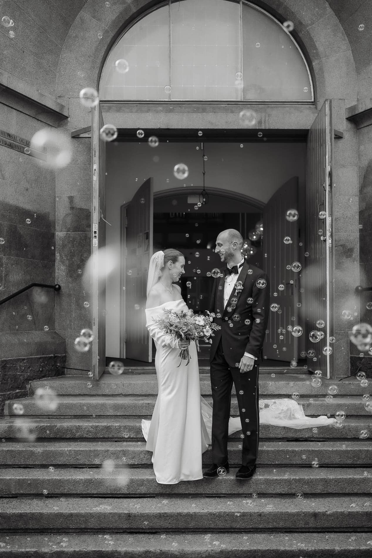 Bryllupspar foran kirke med bobler og smil.