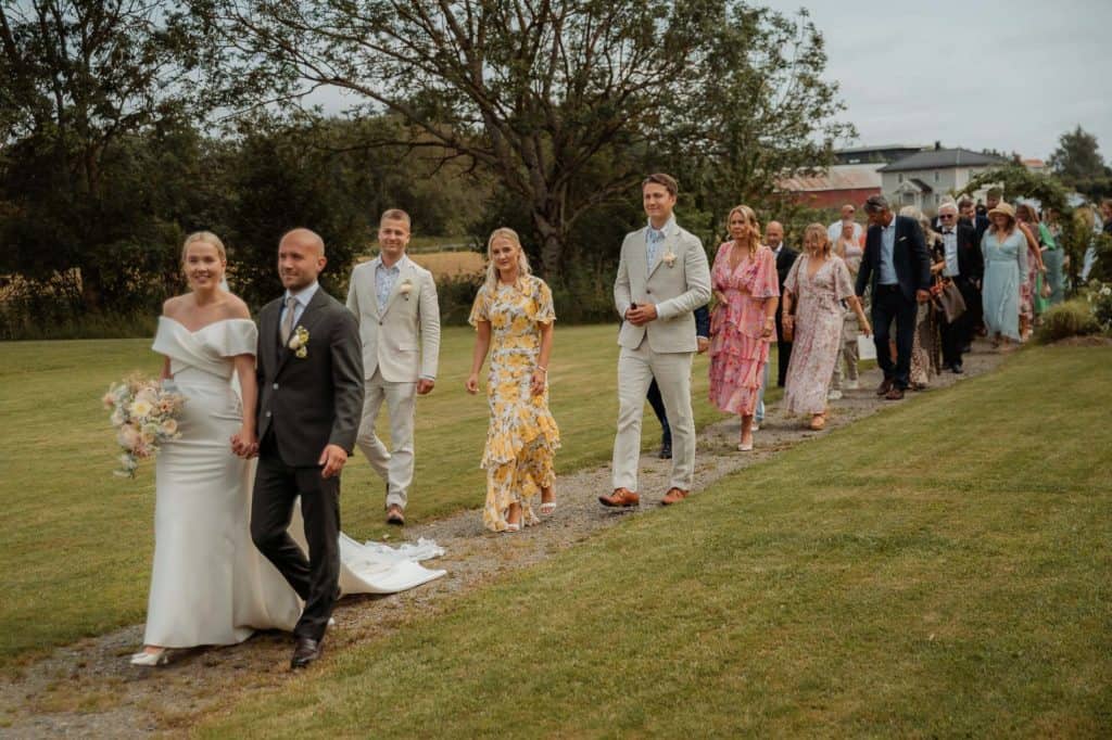 Brudepar og gjester går i bryllupsmarsj på grønt område under bryllupet.