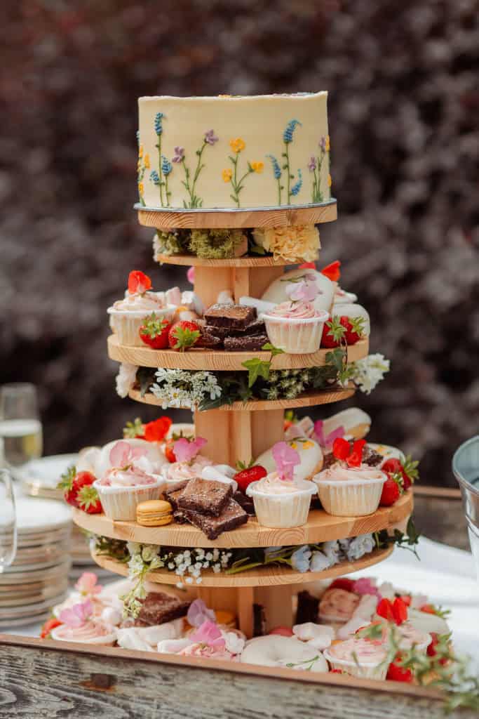 Elegant bryllupskake med blomster og cupcakes på et treetasjes stativ.