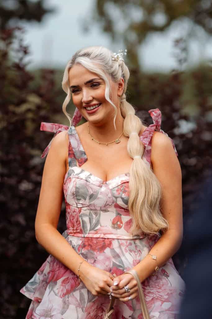 Brud smiler under bryllupet, omgitt av vakre blomster og naturlig bakgrunn.