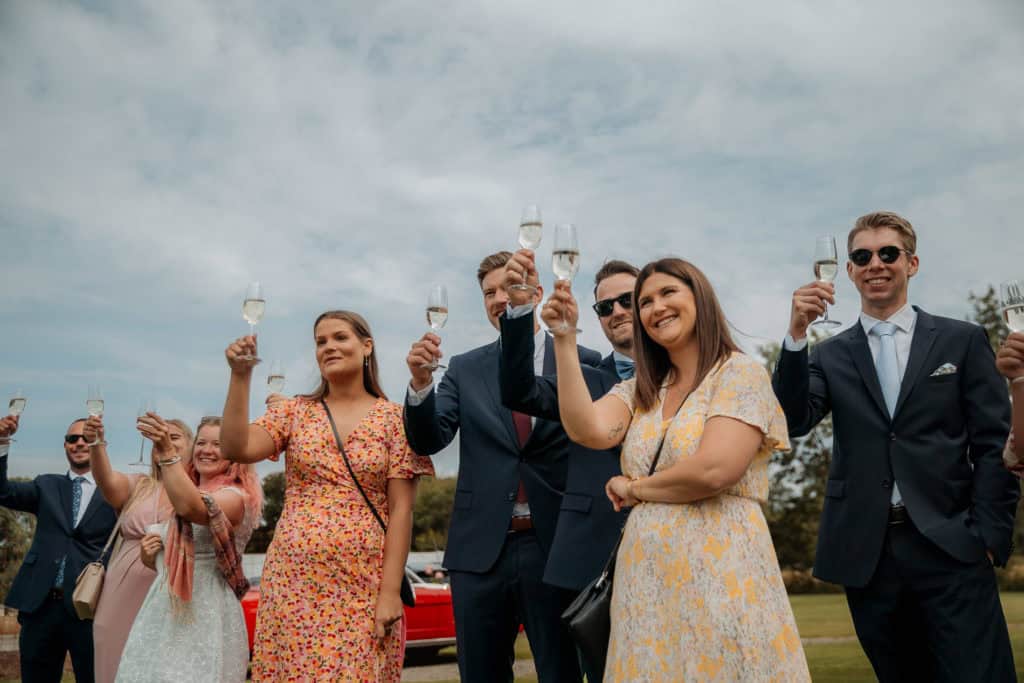 Festglade bryllupsgjester hever glassene i en utendørs seremoni.