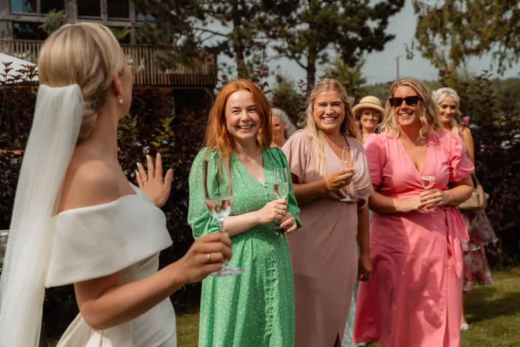 Venner og familie smiler og nyter stemningen under bryllupet utendørs.