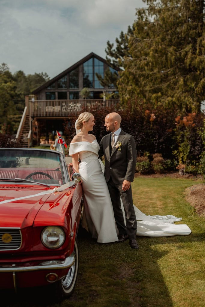 Bryllupsbilder av bruden og brudgommen foran en klassisk bil og moderne hus i naturen.