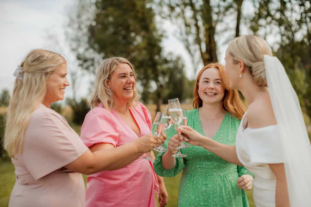 Venner skåler under bryllupet, smilende og glade i utendørs setting.