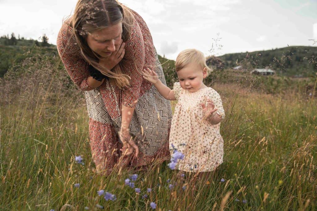Mor og barn utforsker blomster i en åpen eng.