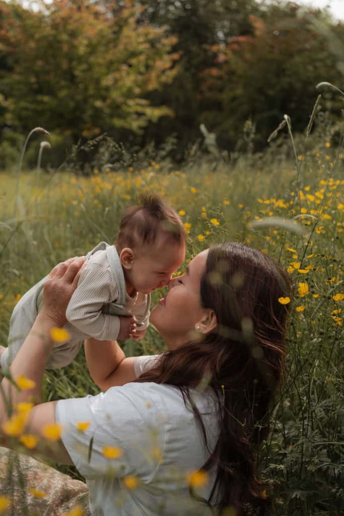 Mor og barn leker i blomstereng med gult og grønt landskap.