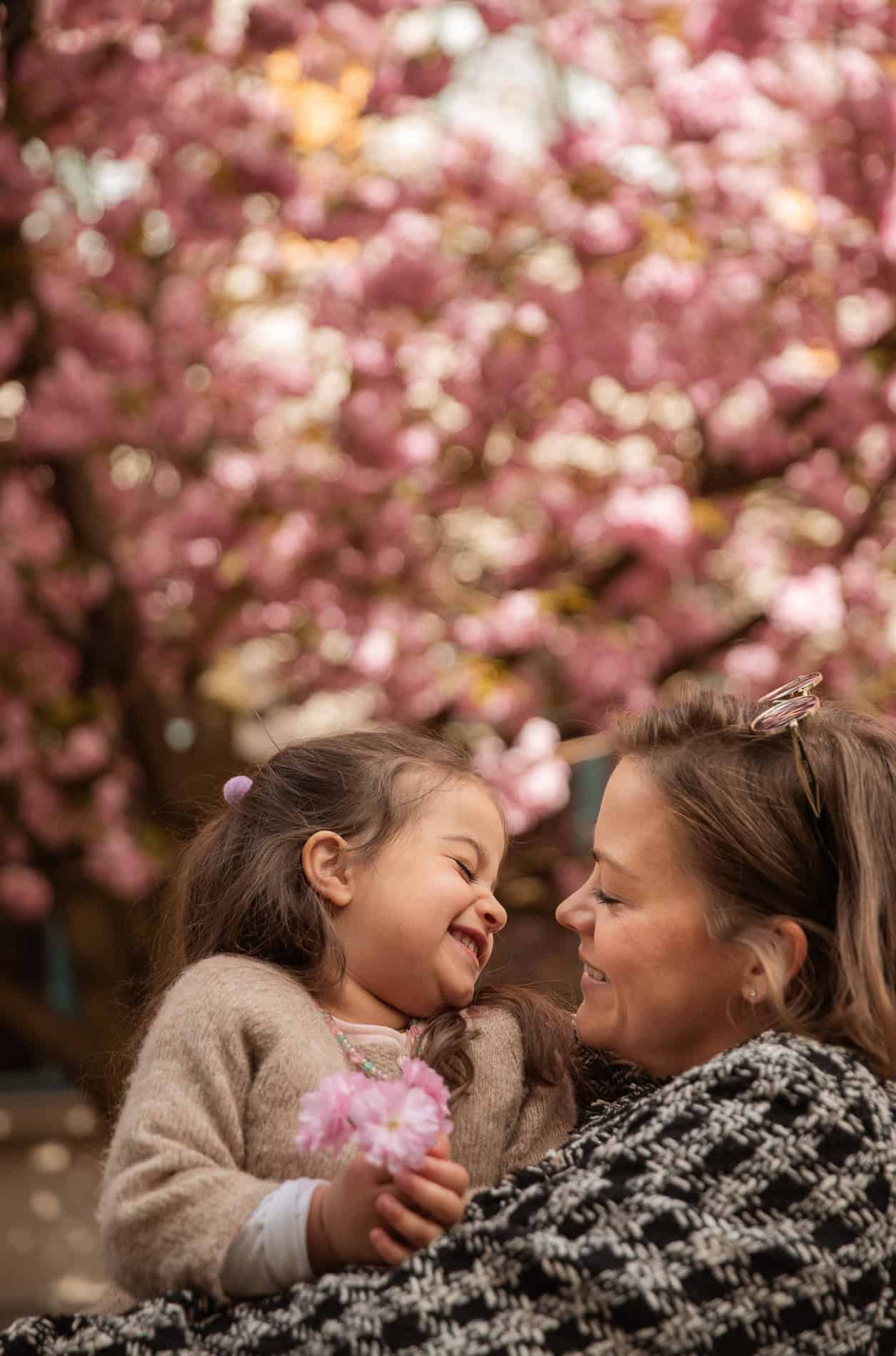 Mor og datter smiler mot hverandre foran blomstrende kirsebærtre.
