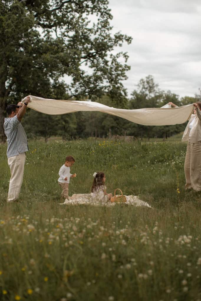Familie leker med stoffduk i grønt landskap med barn og voksne.