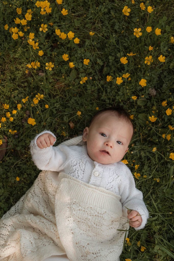 Baby ligger i vugge på blomstereng med gule blomster rundt.