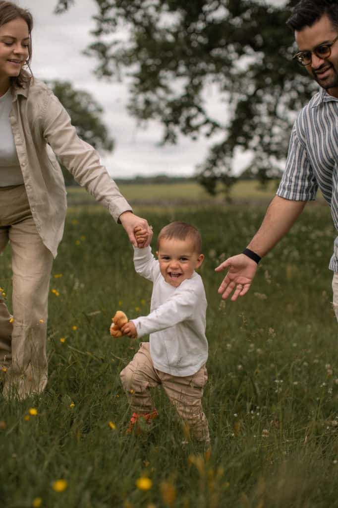 Familie som leker med barnet i en grønn eng med trær i bakgrunnen.