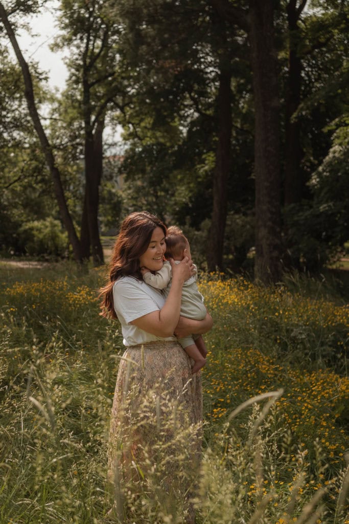 Mor holder sitt barn i en blomstereng i skogen.