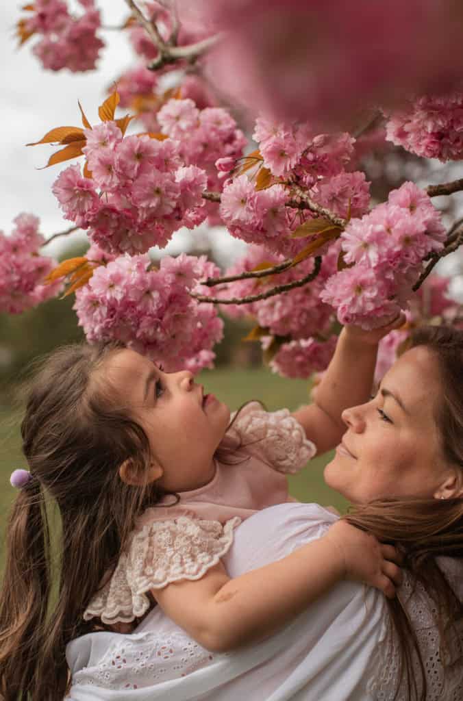 Mor og datter nyter blomstrende kirsebærtre i vårsolen.