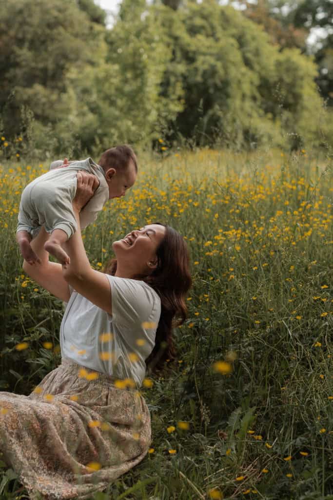 Familie leker i blomstereng med grønt landskap og trær i bakgrunnen.