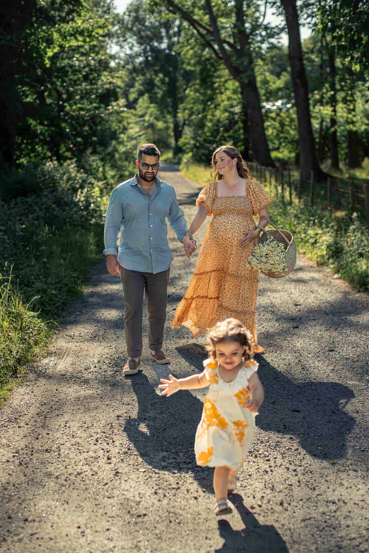 Familie går hånd i hånd på skogssti i solskinn.