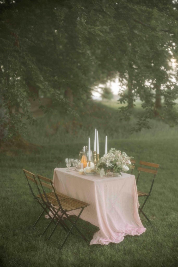 Borddekking i hagen med blomster, lys og elegante glass til utendørs feiring.
