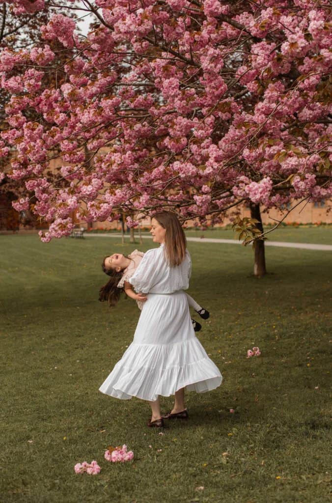 Vakker kvinne danser under et blomstrende kirsebærtre i en park.