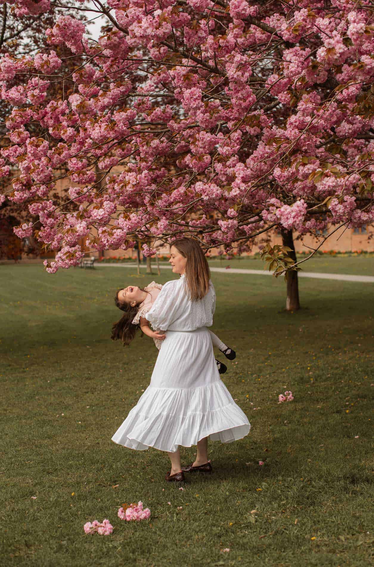 Vakker kvinne danser under et blomstrende kirsebærtre i en park.