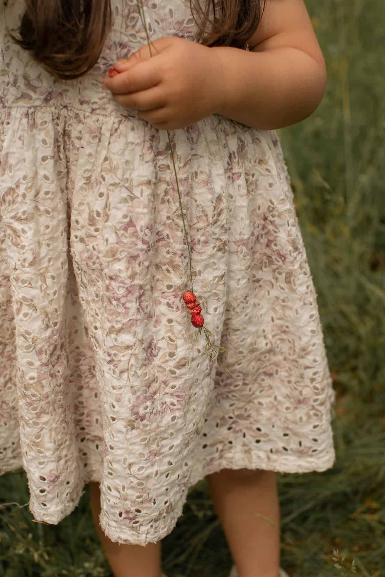 Barn i blomsterkjole holder en liten rød leke, ute i naturen.