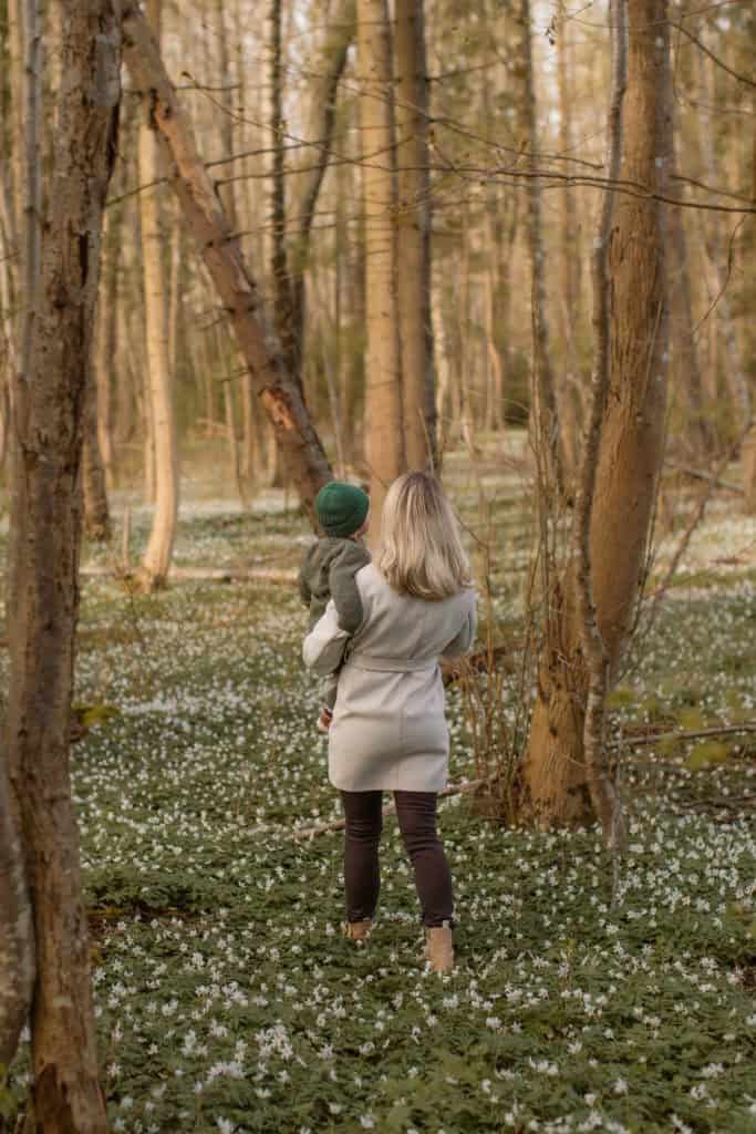 Barn og voksen nyter våren i skogen blant blomstrende trær og markdekorasjoner.